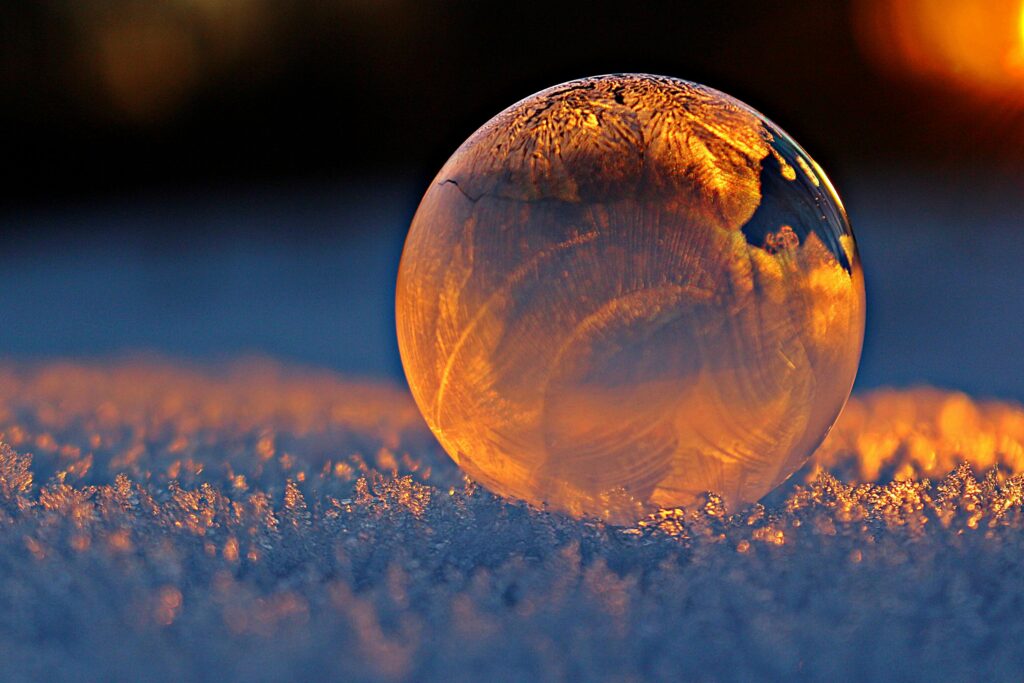 Why has Heavenly Mother been hidden for so long? Close-up shot of a frozen bubble with warm reflections resting on a snowy surface at twilight.